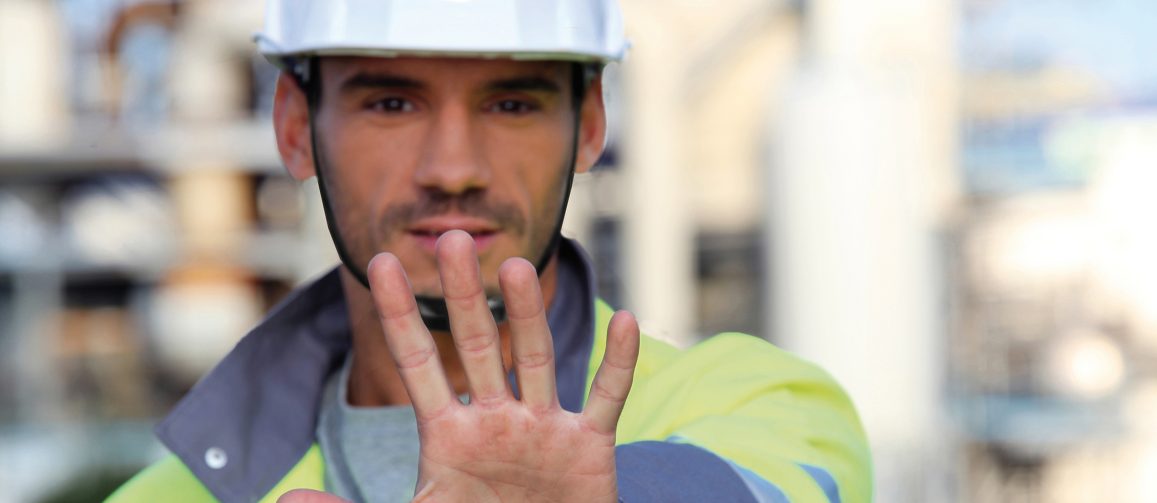 Ein Bauarbeiter mit Schutzhelm hält seine linke Hand hoch als Stopp-Zeichen