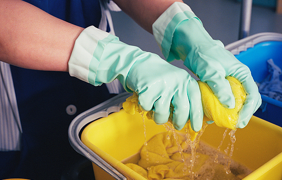 Abwaschen mit Handschuhen und Lappen über einem wassergefüllten Eimer.
