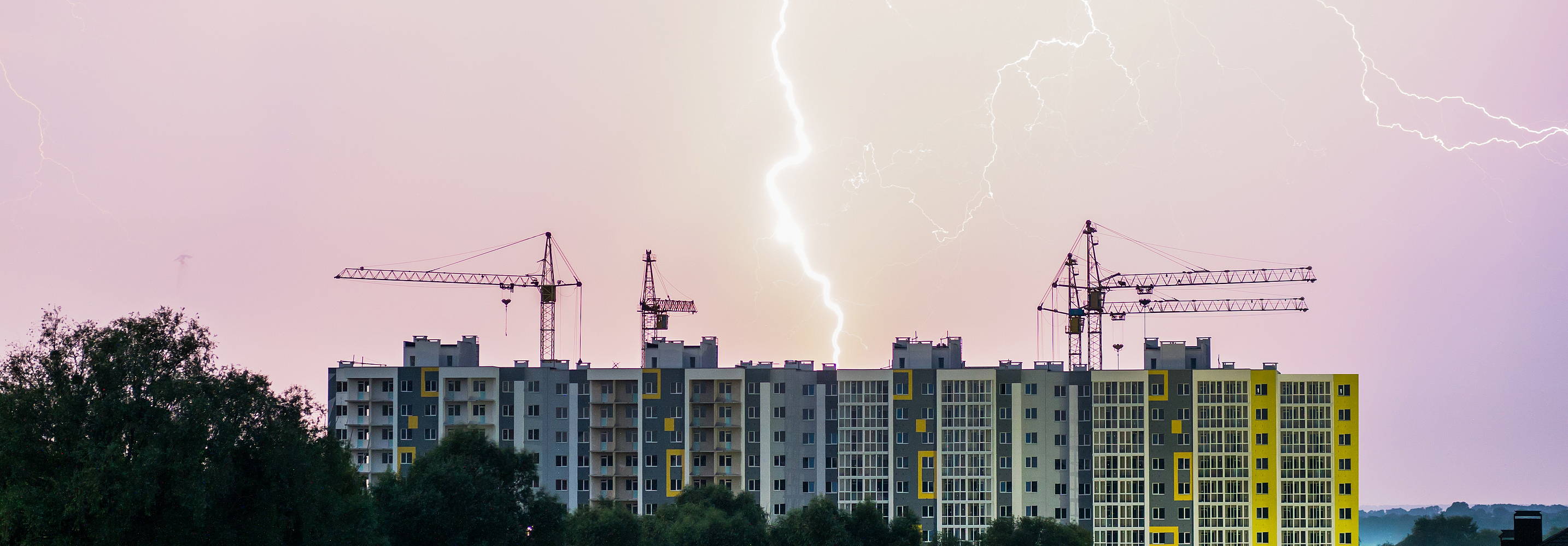 Ein Unwetter mit Blitzen zieht über einem Wohnblock und einer Baustelle auf.