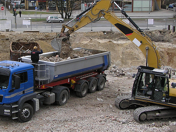 Ein LKW wird auf einer Baustelle von einem Bagger beladen