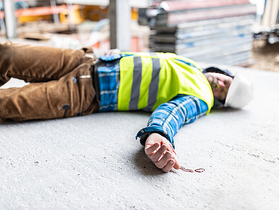 Ein Mann in Arbeitskleidung liegt verunfallt auf dem Boden