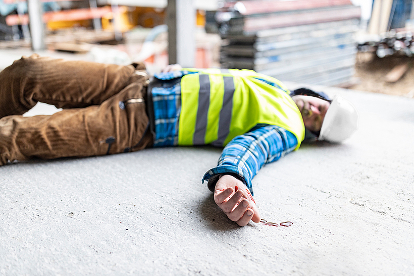 Ein Mann in Arbeitskleidung liegt verunfallt auf dem Boden