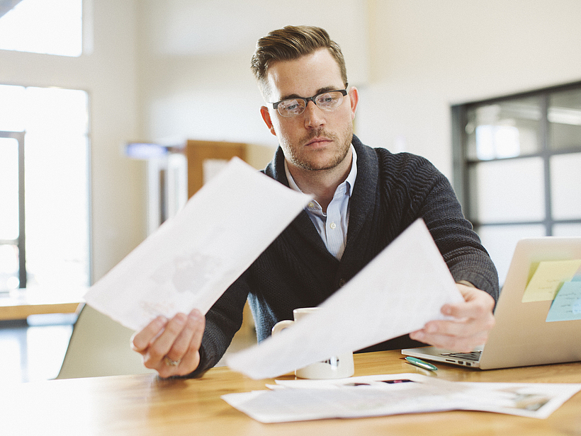 Ein Mann sitzt in einem Büro am Laptop und liest ein Schreiben.