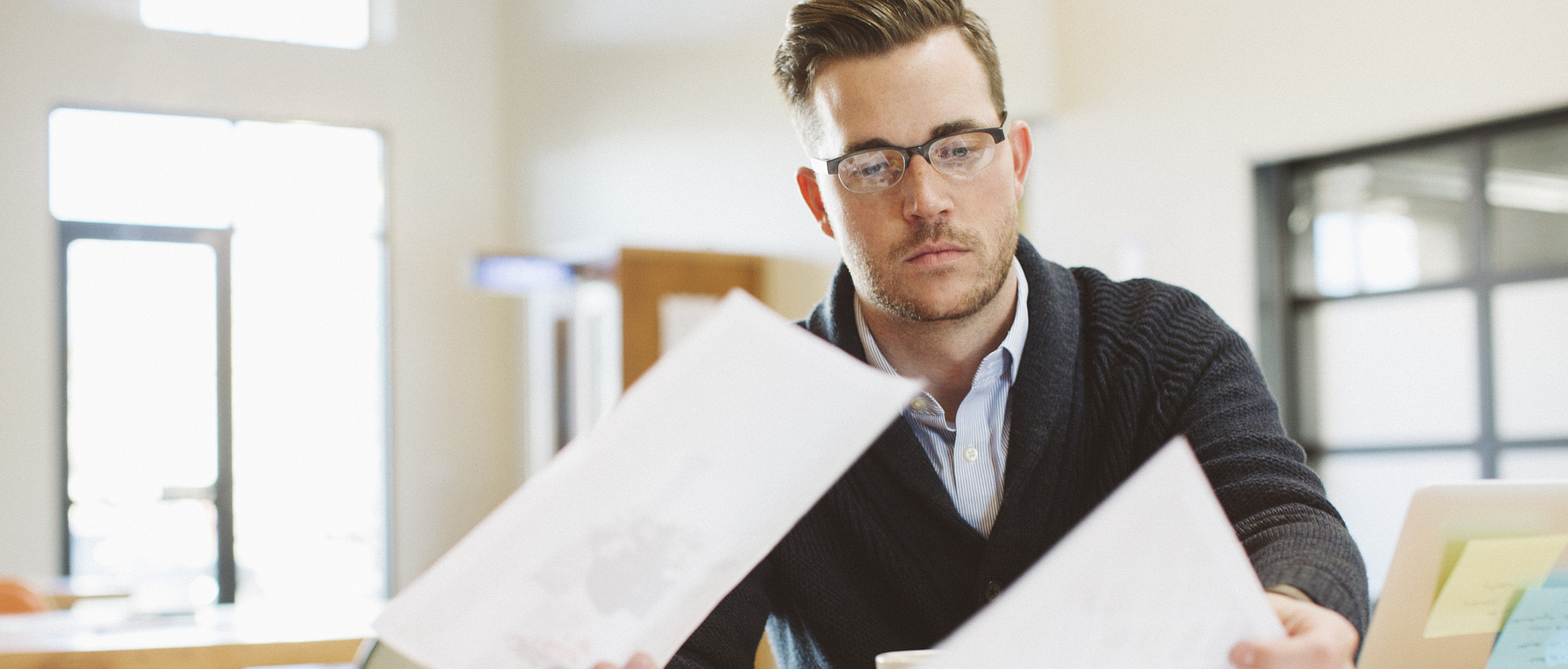 Ein Mann sitzt in einem Büro am Laptop und liest ein Schreiben.