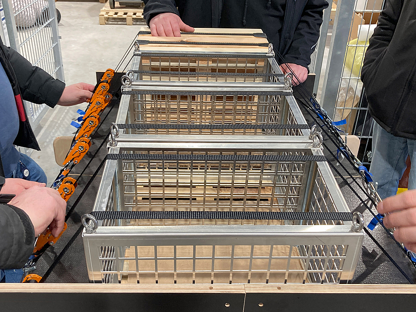 Mehrere Personen sichern Gitterboxen auf einer Ladefl&auml;che mit Spanngurten und Ratschen zur fachgerechten Ladungssicherung.