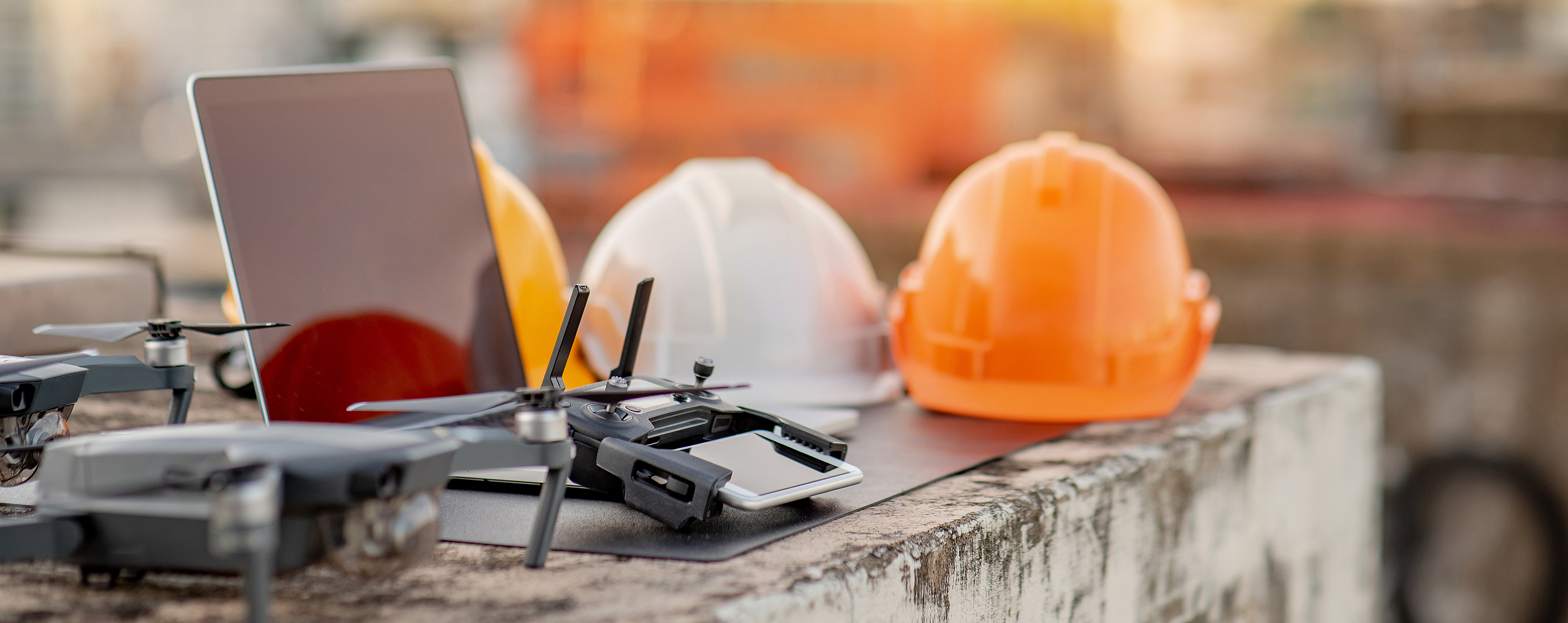 Drohne, Smartphone, Laptop und Schutzhelm auf einer Baustelle. Einsatz von unbemannten Luftfahrzeugen (UAV) für Land- und Baustellenuntersuchungen in Tiefbauprojekten.