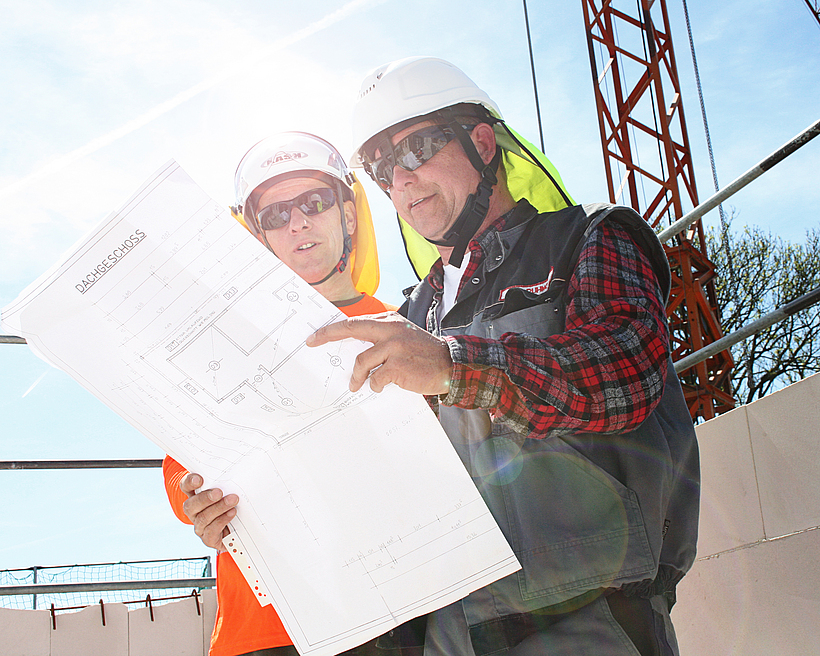 Eine Aufsichtsperson und ein Unternehmer sind in einem Gespräch auf einer Baustelle. 