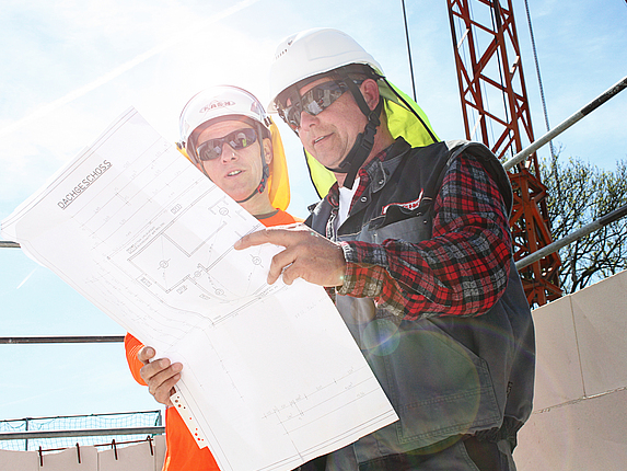 Eine Aufsichtsperson und ein Unternehmer sind in einem Gespräch auf einer Baustelle. 
