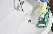 Eine Person reinigt mit einem flexiblen Handwischer die runden Ecken eines Waschbeckens