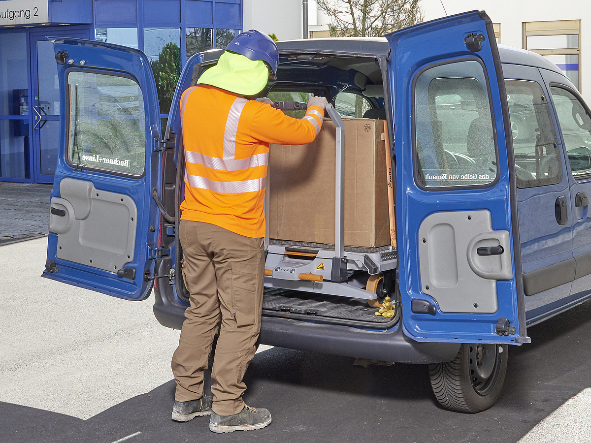 Ein Mann bel&auml;dt die Last vollst&auml;ndig in das Fahrzeug mithilfe eines elektrohydraulischen Systems des Transportwagens mit Hebehilfe 