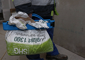 Ein Mann trägt in aufrechter Körperhaltung einen Trage- und Verschlussgriff angebrochener Sackware