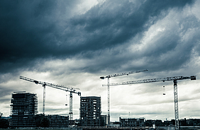 Eine Hochbaustelle mit Kränen unter wolkenbedecktem Himmel. 