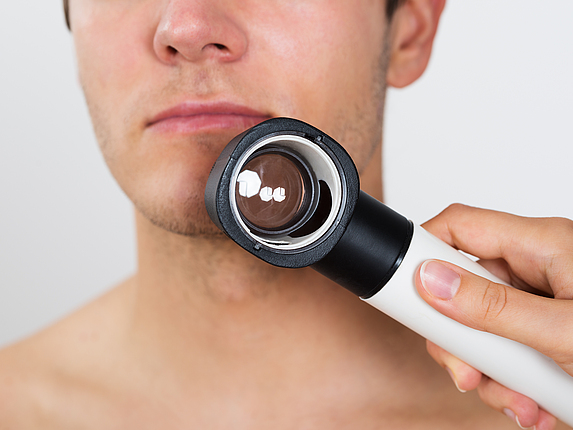 Das Gesicht eines Mannes wird beim Hautkrebs-Screening mit einer Lupe untersucht.