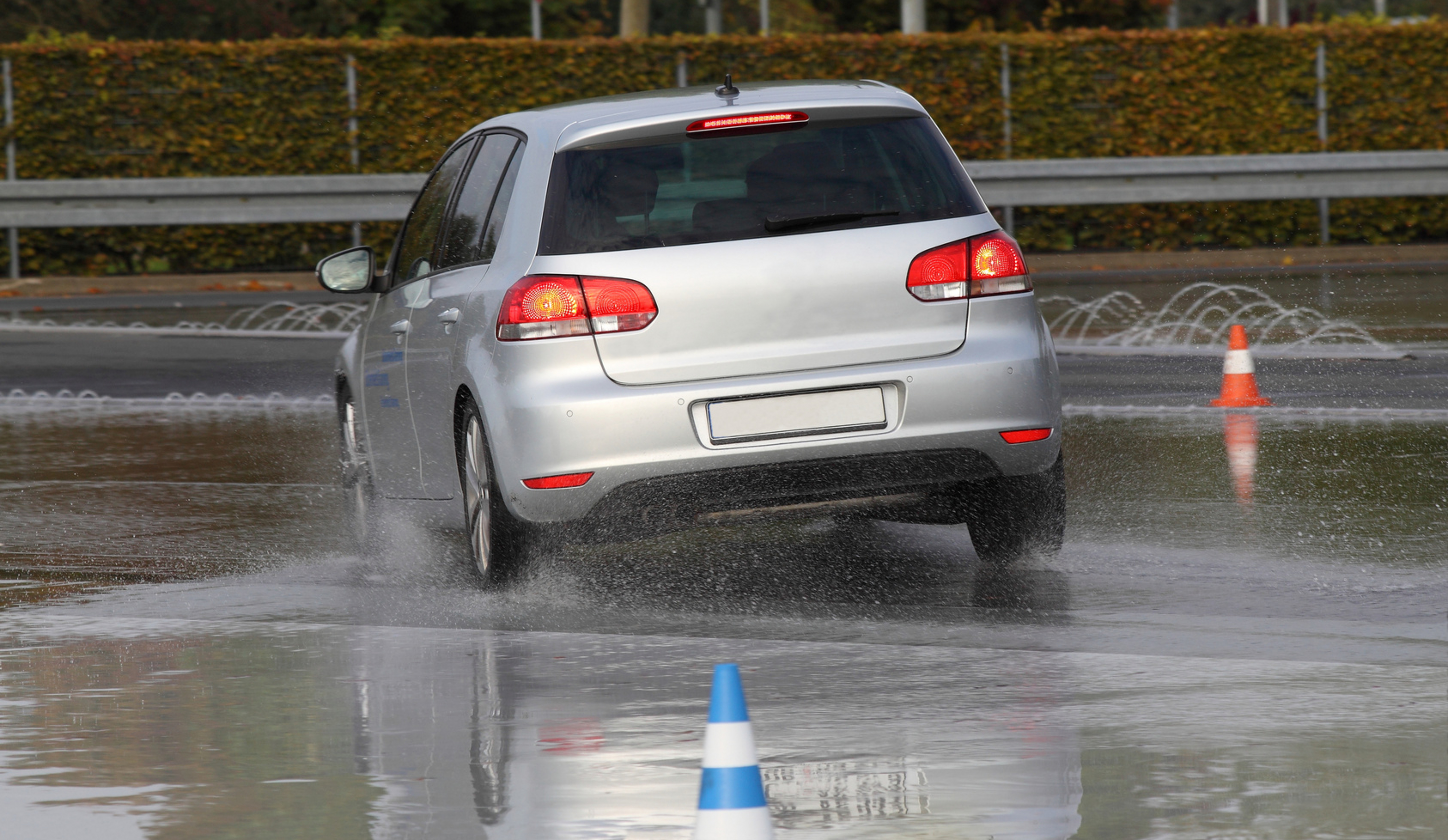 Ein Auto f&auml;hrt auf einer nassen Stra&szlig;e, auf der zwei Leitkegel aufgestellt sind.