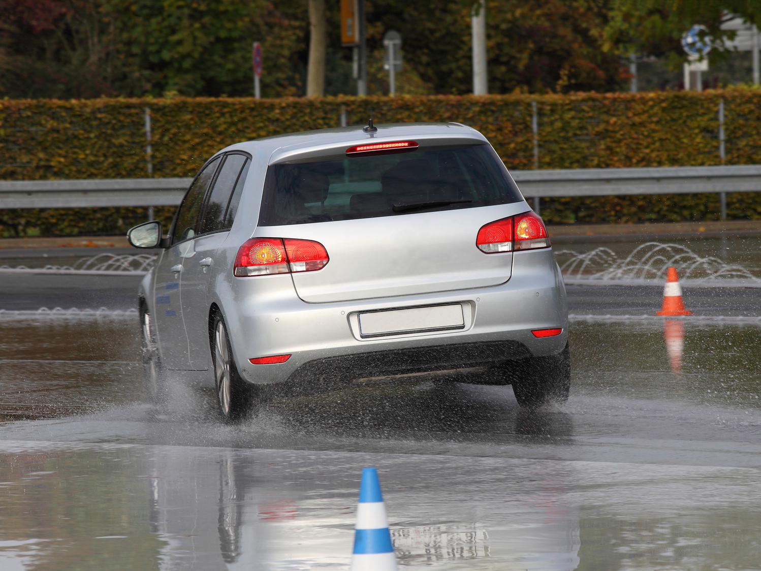 Ein Auto fährt auf einer nassen Straße, auf der zwei Leitkegel aufgestellt sind.