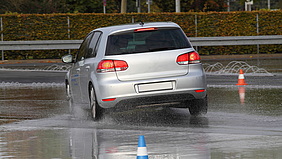 Ein Auto fährt auf einer nassen Straße, auf der zwei Leitkegel aufgestellt sind.