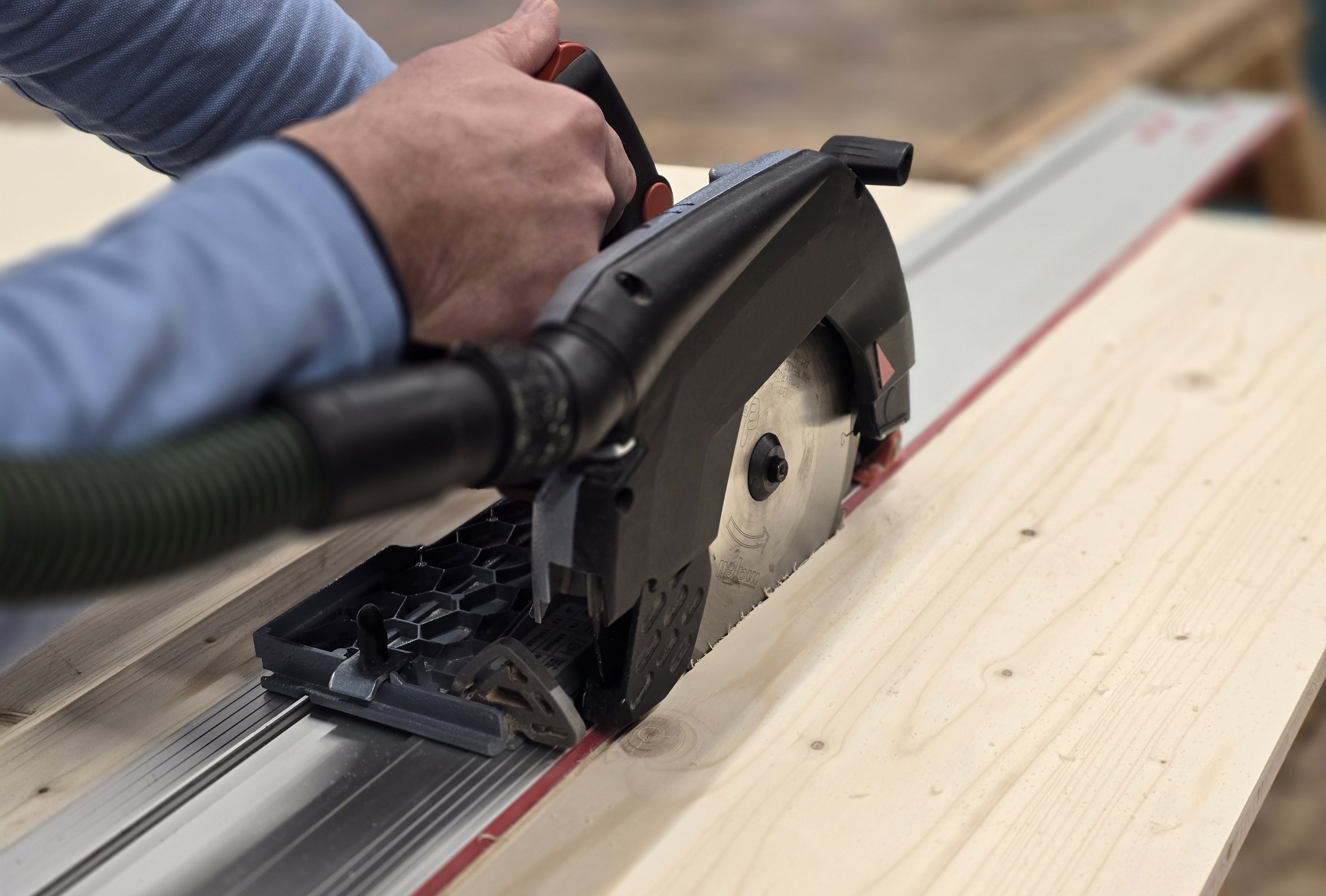 Zwei Hände führen eine Handkreissäge, die Holz durchtrennt.