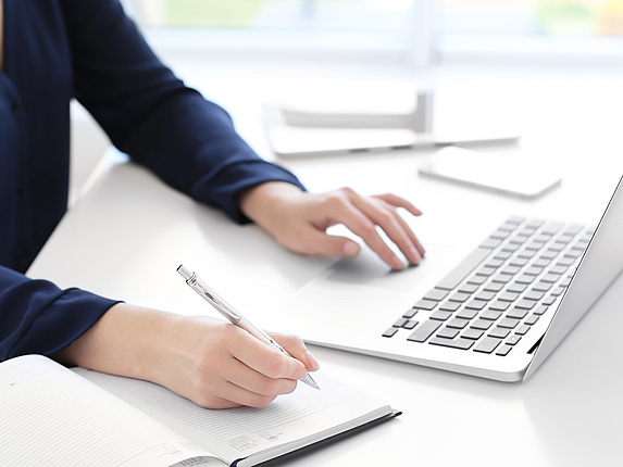 Junge Frau, die am Schreibtisch einen Laptop für die Suche von Informationen im Internet verwendet