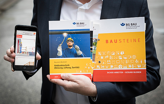 Eine Person hält ein Handy in der Hand mit der Bausteine App, dem Baustein Ordner und Baustein Merkhefte.