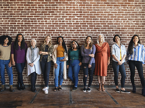 Eine Gruppe von Frauen, die an der Wand gelehnt stehen und lächeln.