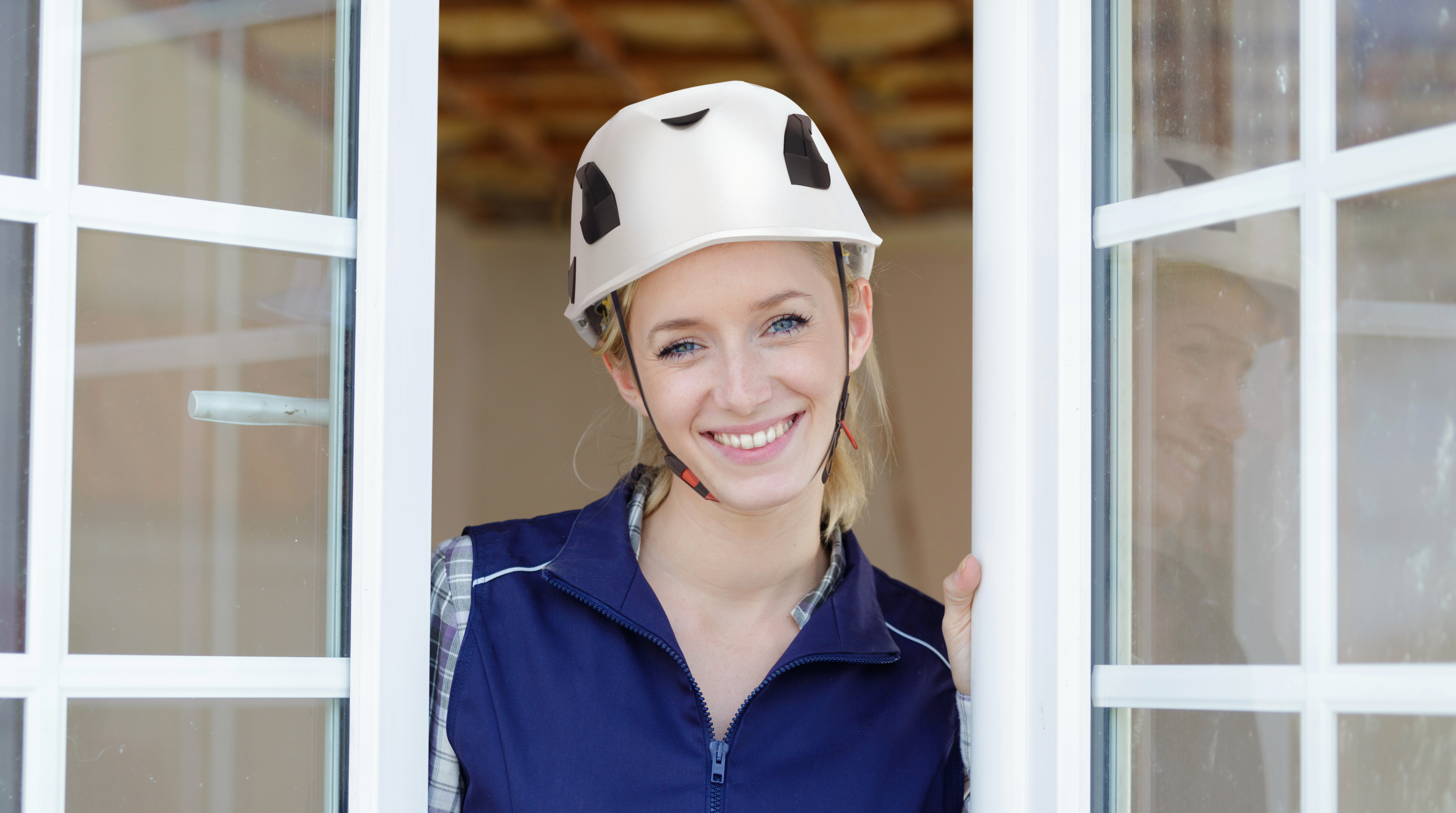 Eine junge Bauarbeiterin mit einem Schutzhelm blickt durch das geöffnete Fenster.