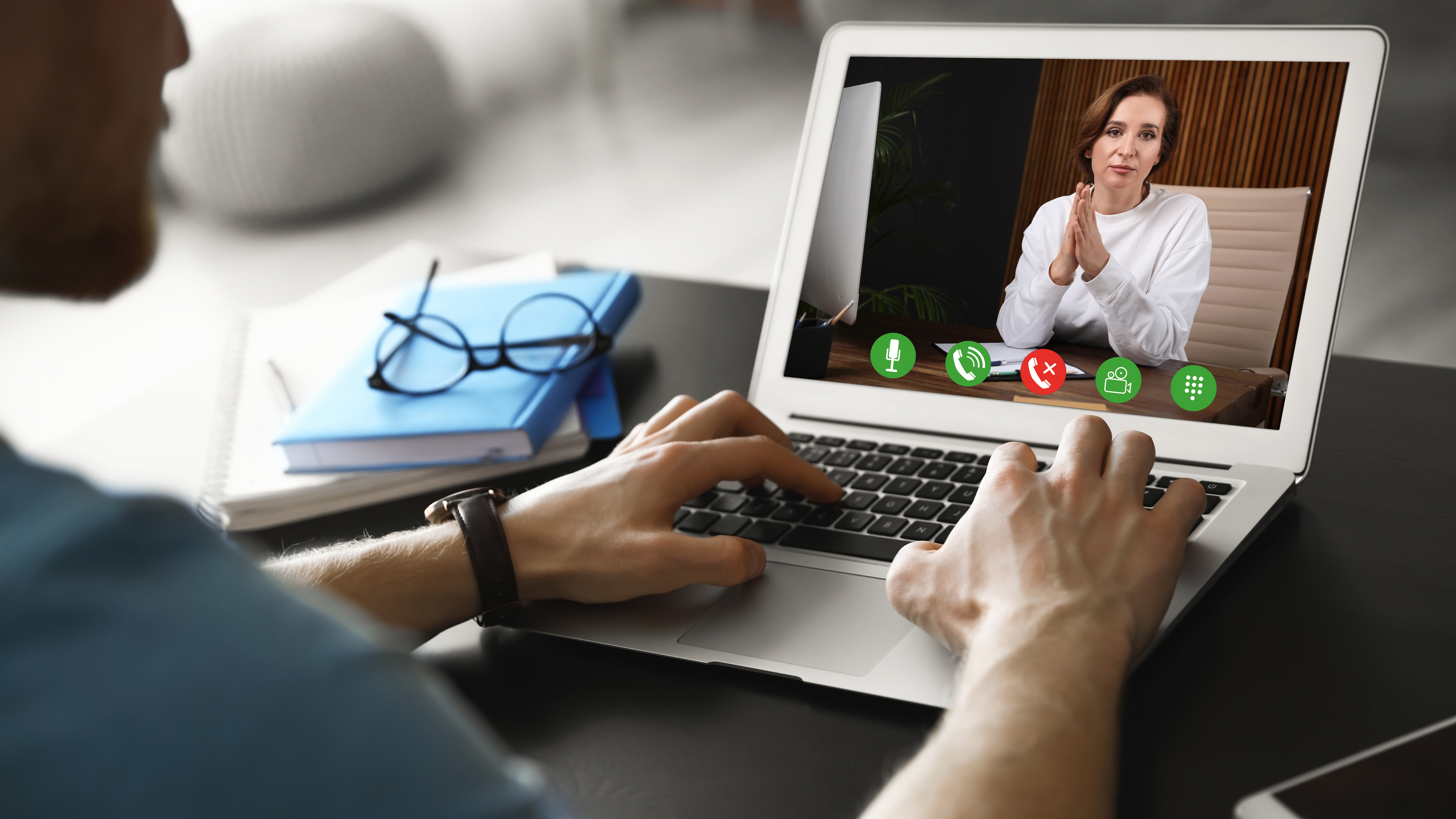 Ein Mann sitzt am Schreibtisch mit einem Laptop. Er führt eine Videokonferenz mit einer Frau. 