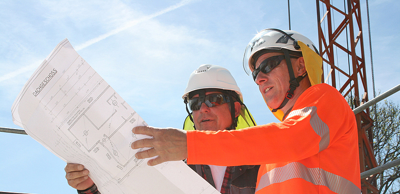 Aufsichtsperson mit Vier-Punkt-Kinnriemen am Schutzhelm und Nackenschutz auf einer Baustelle.