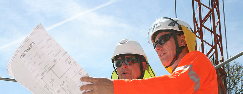 Aufsichtsperson mit Vier-Punkt-Kinnriemen am Schutzhelm und Nackenschutz auf einer Baustelle.