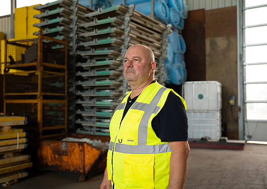 Lothar Hubert steht mit einer gelben Warnweste in einer Lagerhalle.