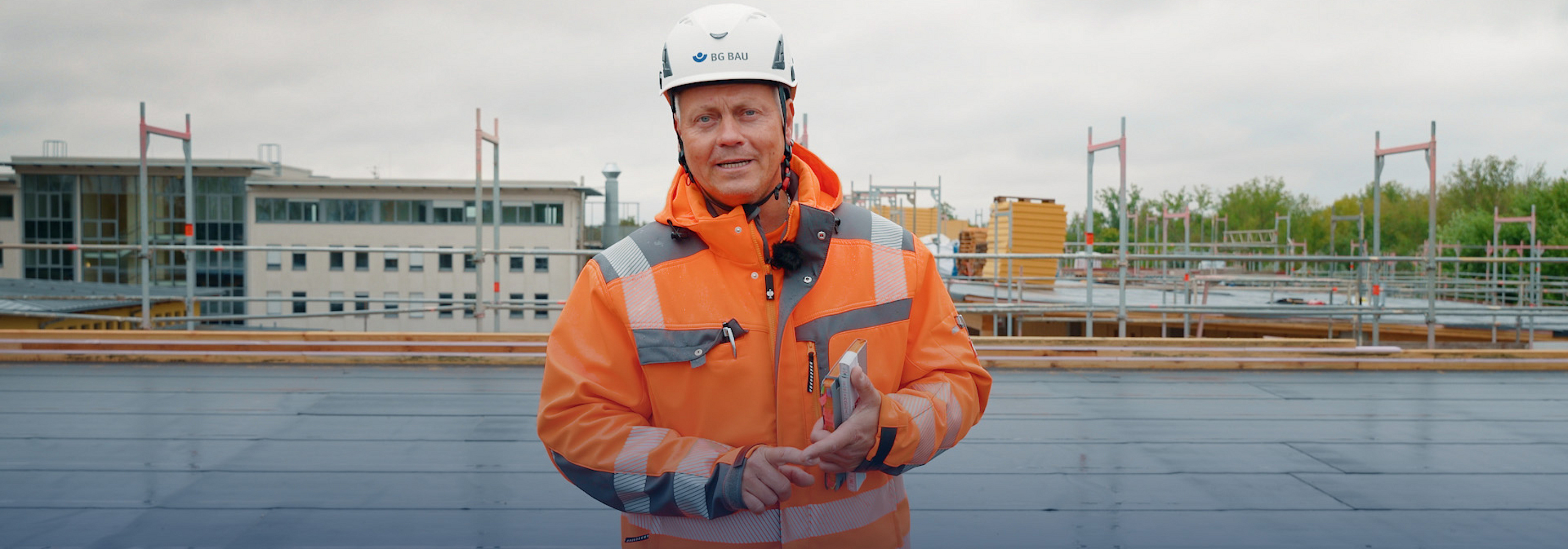 BG BAU Aufsichtsperson Denny Hillert steht mit Helm und Schutzkleidung auf einem Dach.