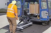 Ein Mann l&auml;dt einen Karton &uuml;ber das integrierte elektrohydraulische System des Transportwagens mit Hebehilfe (xetto) in ein Fahrzeug hinein