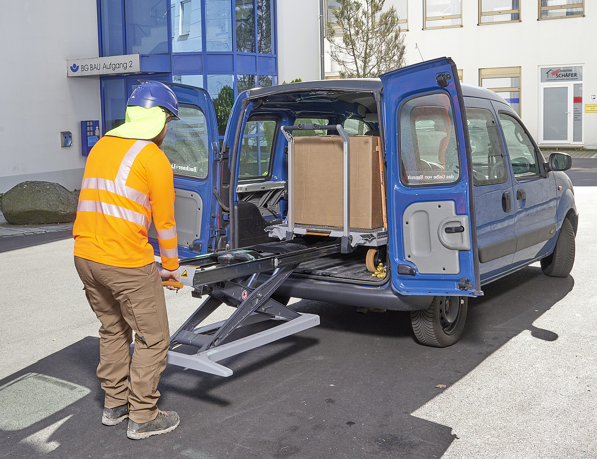 Ein Mann lädt einen Karton über das integrierte elektrohydraulische System des Transportwagens mit Hebehilfe (xetto) in ein Fahrzeug hinein