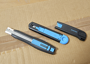 Drei Sicherheitsmesser liegen auf einem Karton.