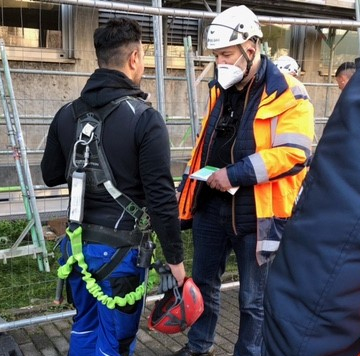 Eine Aufsichtsperson im Gespräch mit einem Bauarbeiter während einer Baustellenbesichtigung