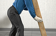 Mann mit schwerem Holzbalken verdeutlicht das rückenschonende Heben und Tragen schwerer Lasten 