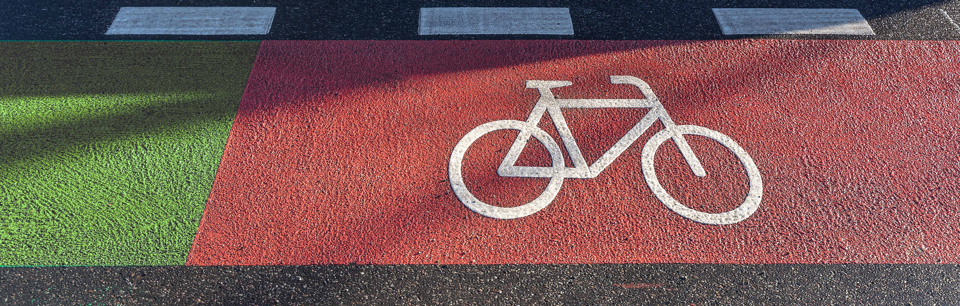 Roter Fahrradweg auf einer Straße. Daneben fährt ein Auto.